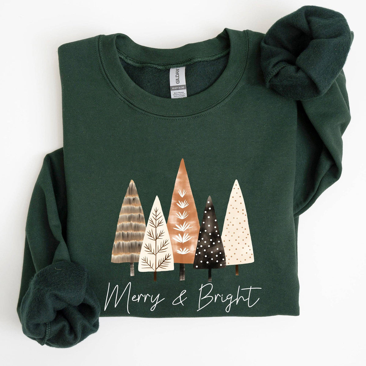 Folded green sweatshirt with Christmas tree design and 'Merry & Bright' text on a white background