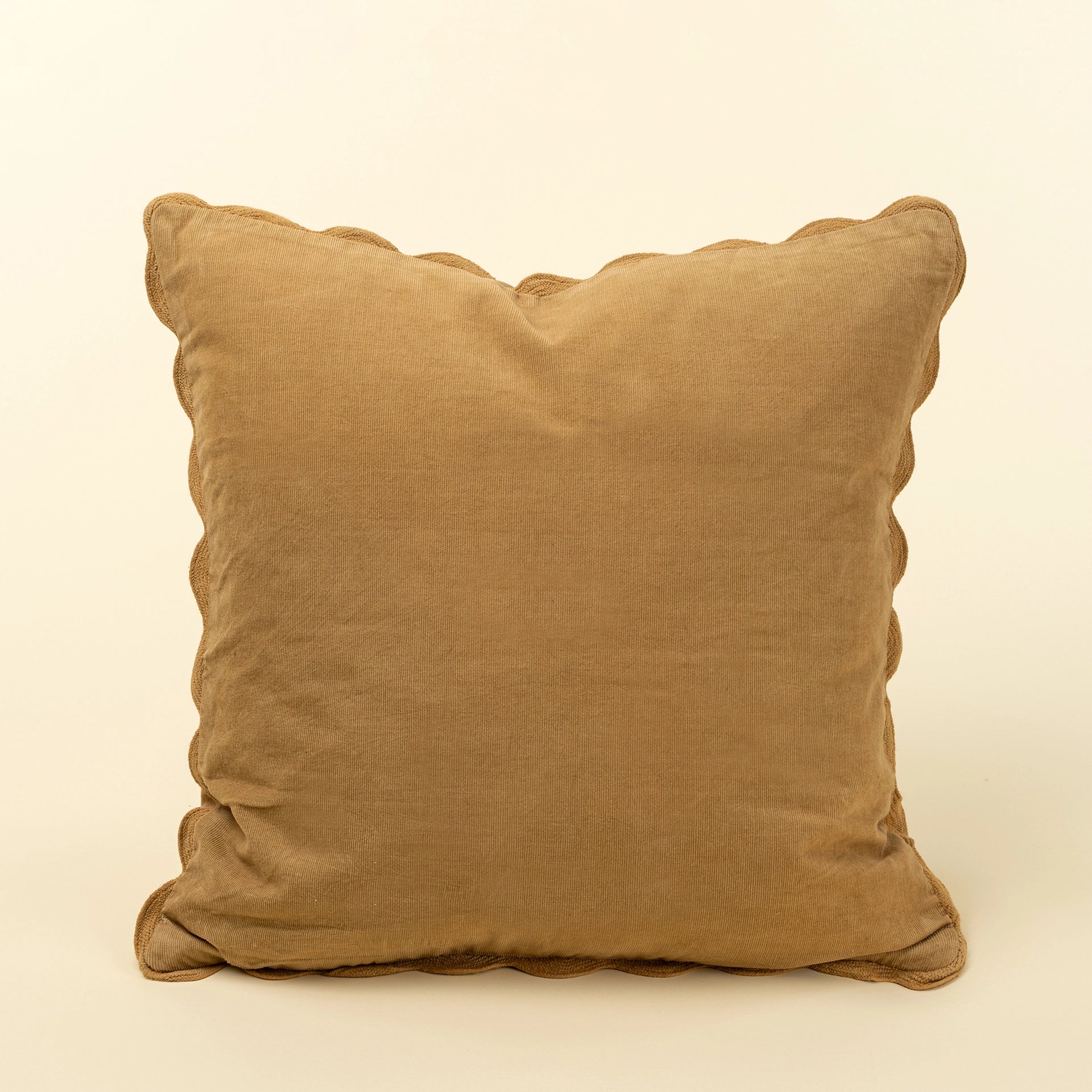 A square tan linen throw pillow with scalloped edges, photographed against a solid cream background at the rustic barn in killingworth ct