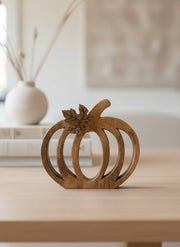 A small carved wooden pumpkin decoration with a leaf and stem, displayed on a light wood table in a softly blurred indoor setting.