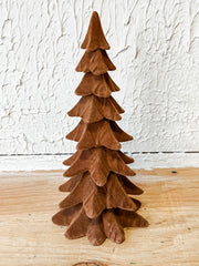 A small decorative tree made from layered brown felt or suede-like material, standing on a light wood surface against a textured white wall at the rustic barn in killingworth ct