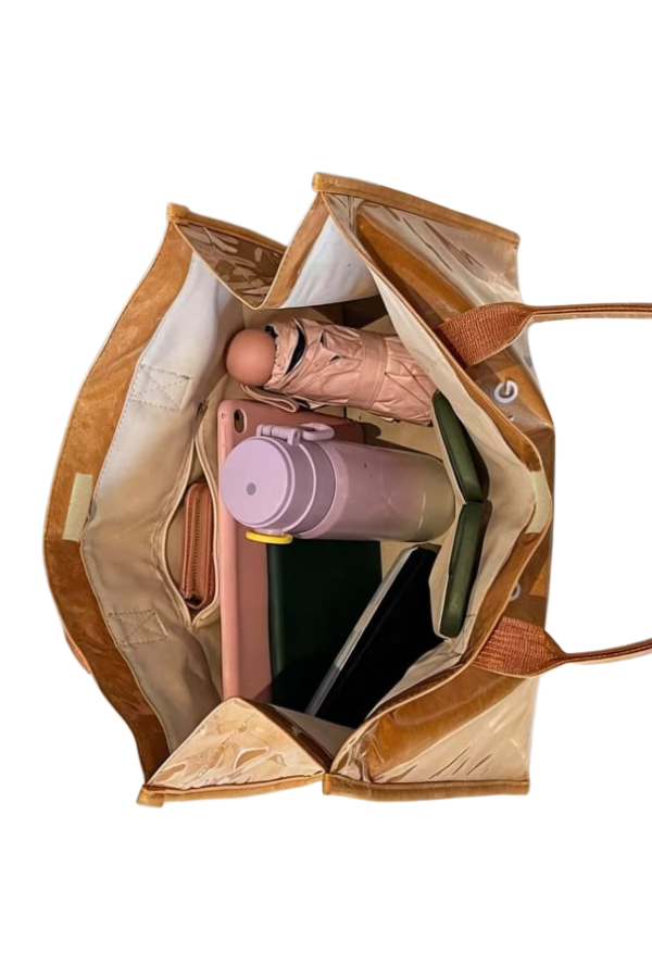 Open brown leather handbag with pink water bottle and green book on a white background