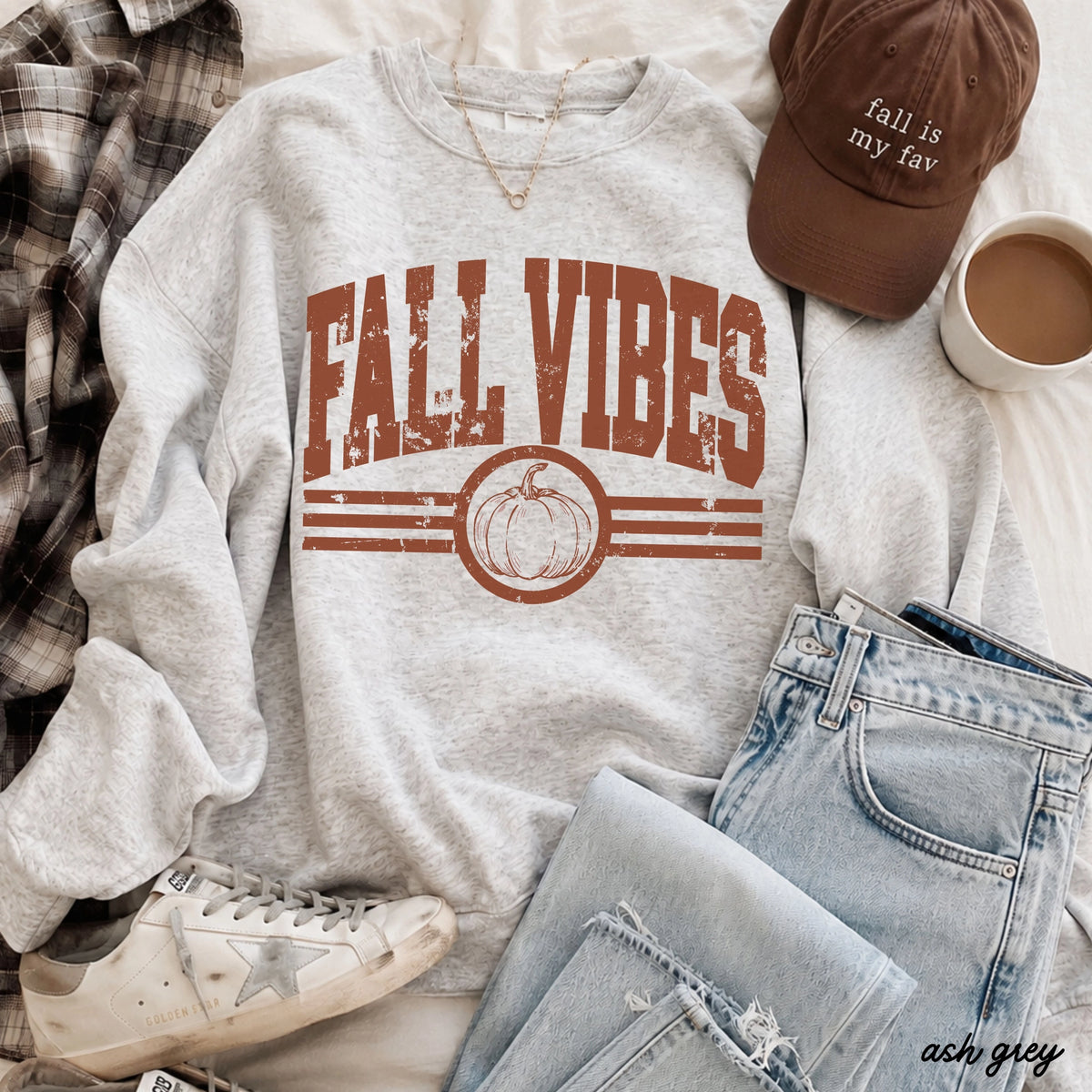 Gray sweatshirt with 'Fall Vibes' print, brown cap, plaid shirt, jeans, and coffee cup on a light background at the rustic barn in killingworth ct