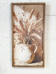 A framed rustic still life wall art print depicting dried wheat stalks in a white ceramic pitcher, mounted on a textured white wall at the rustic barn in killingworth ct