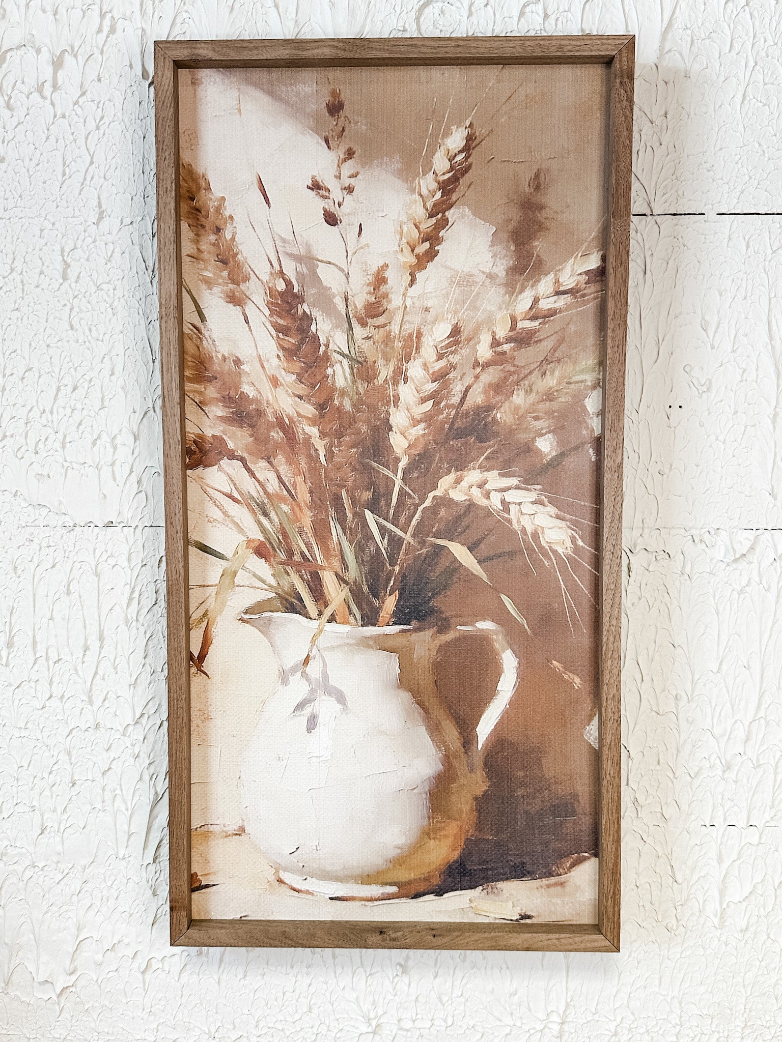 A framed rustic still life wall art print depicting dried wheat stalks in a white ceramic pitcher, mounted on a textured white wall at the rustic barn in killingworth ct