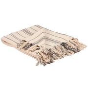 A beige and gray striped cotton throw blanket with tassels on the edges, folded and placed on a flat surface at the rustic barn in killingworth ct