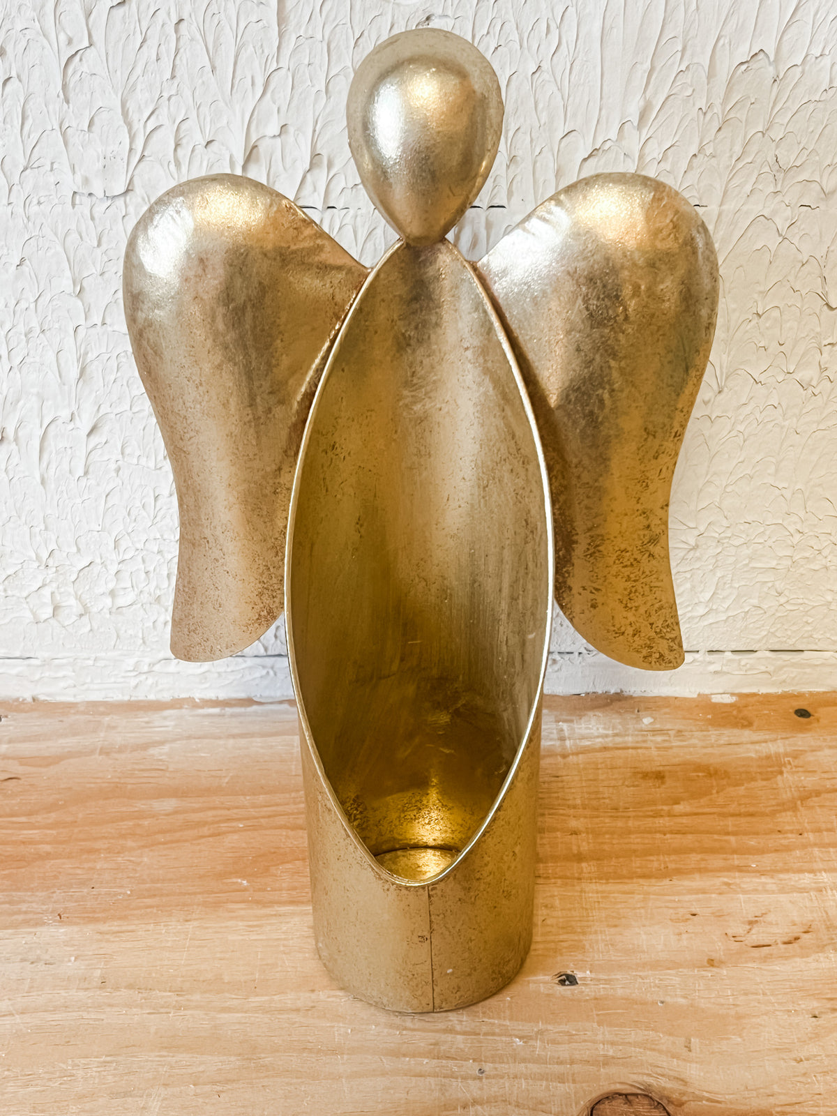 A metallic gold angel-shaped planter with a textured finish, standing on a light wood surface against a white textured wall at the rustic barn in killingworth ct