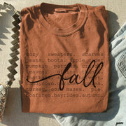 A folded terracotta brown t-shirt with a dark graphic print reading 'cozy sweaters. scarves jeans at the rustic barn in killingworth ct