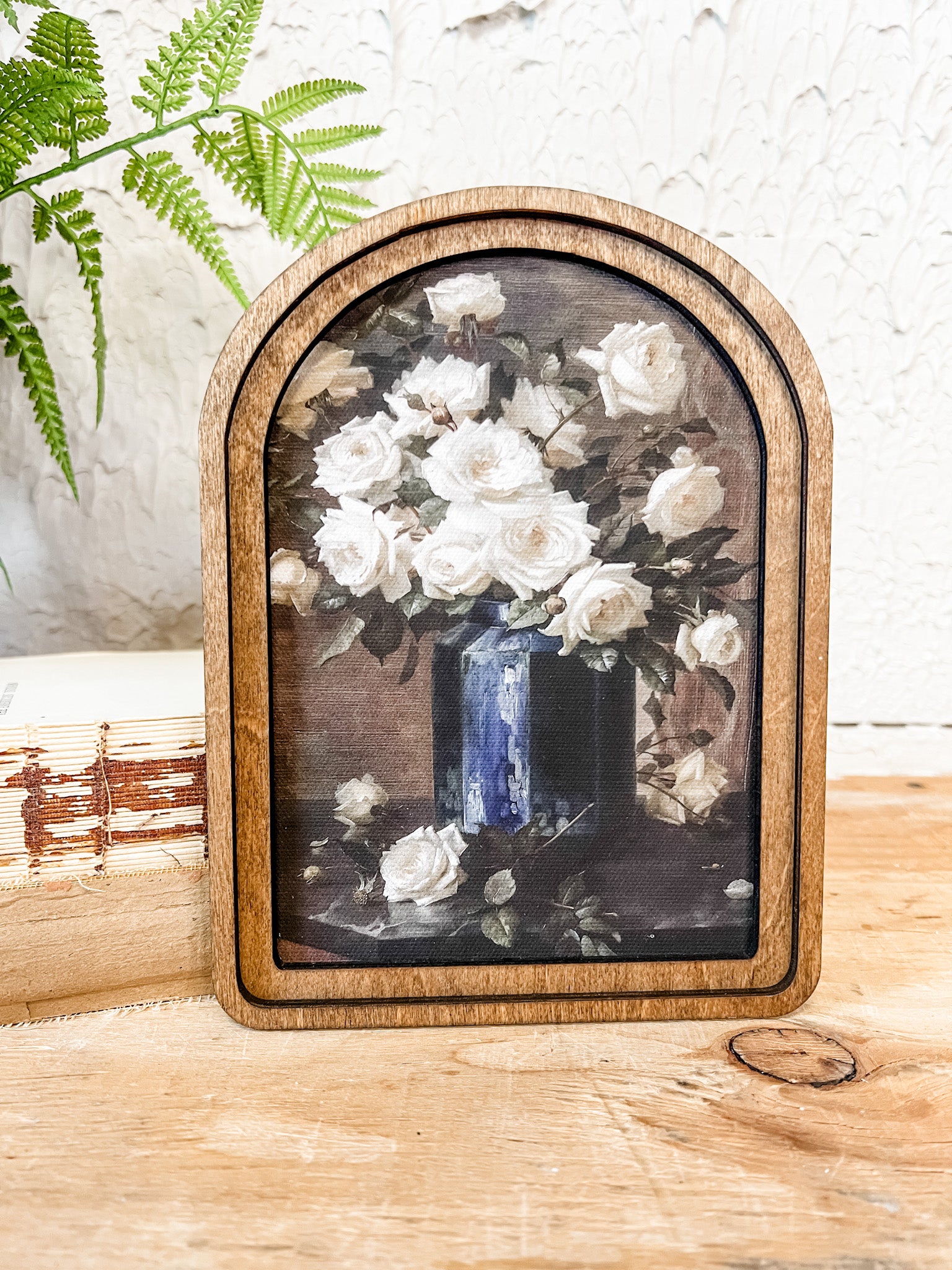 Framed artwork of white flowers in a blue vase on a wooden surface with a white textured wall background at the rustic barn in killingworth ct