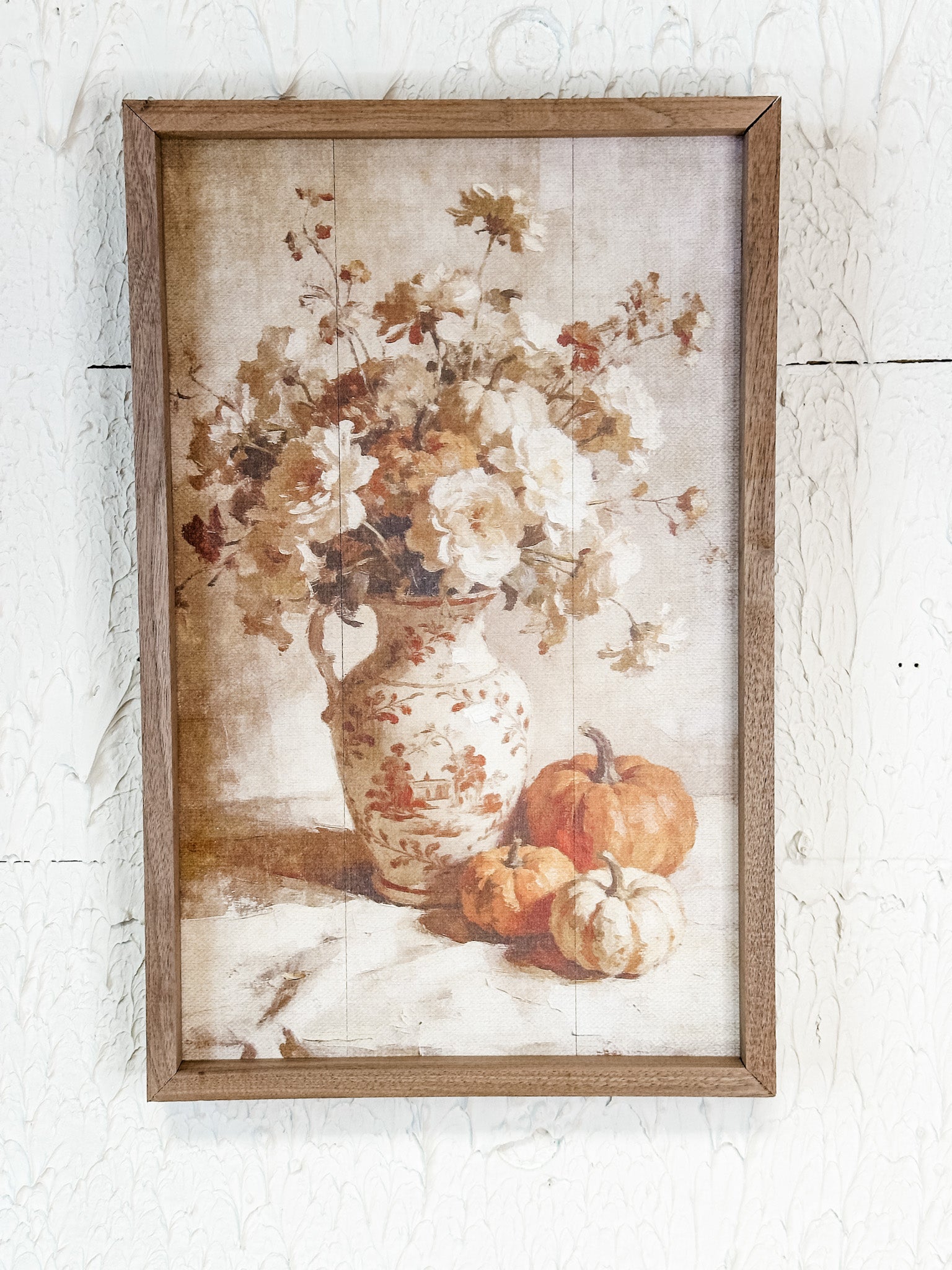 A framed rustic still life wall art print featuring a floral arrangement in a patterned vase with pumpkins, hung on a white textured wall.  At The Rustic Barn in Killingworth Ct