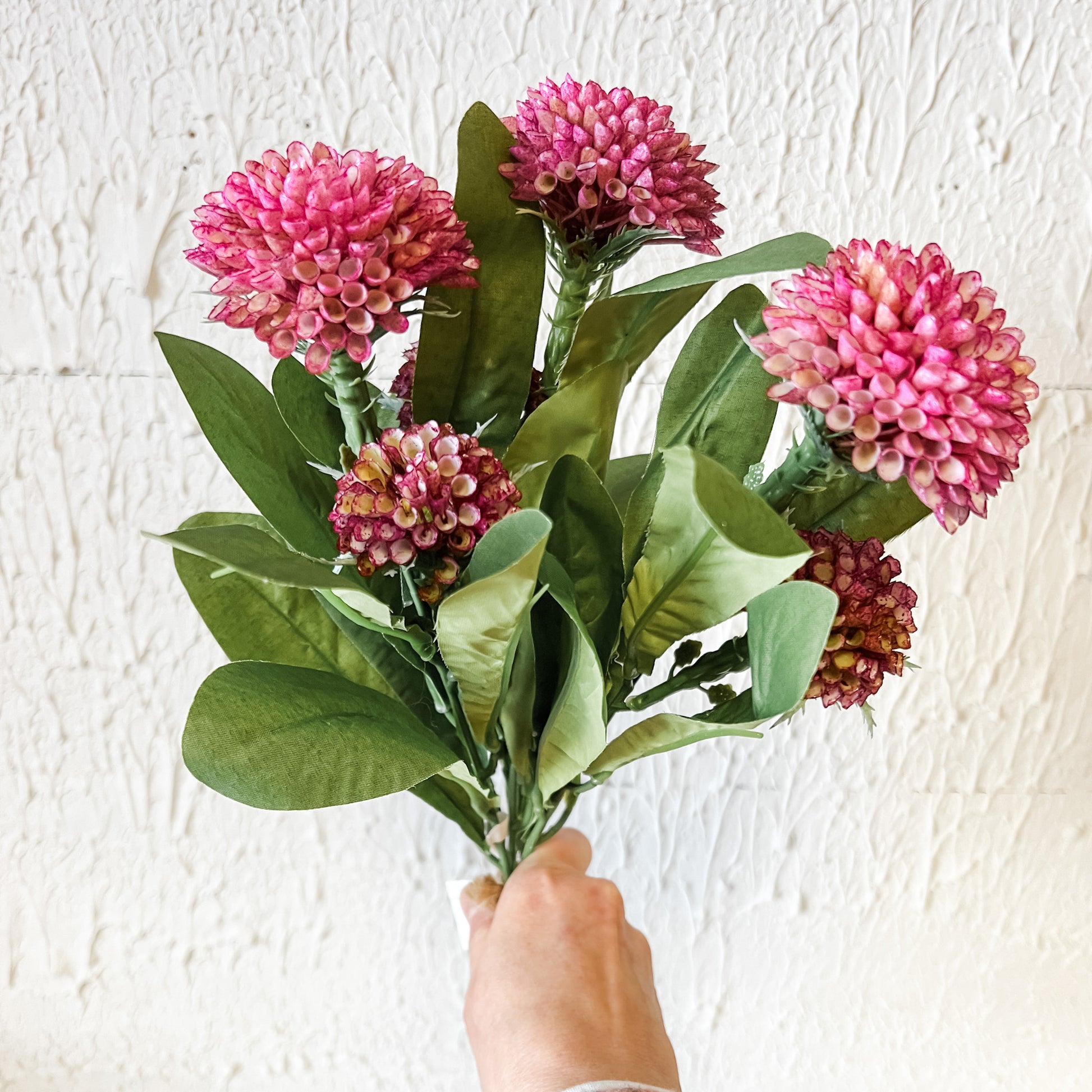 Bouquet of pink flowers held against a white textured wall
