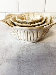 A set of nested ceramic bowls with a ribbed, lotus-petal design, shown on a gray stone surface with a white tiled background at the rustic barn in killingworth ct