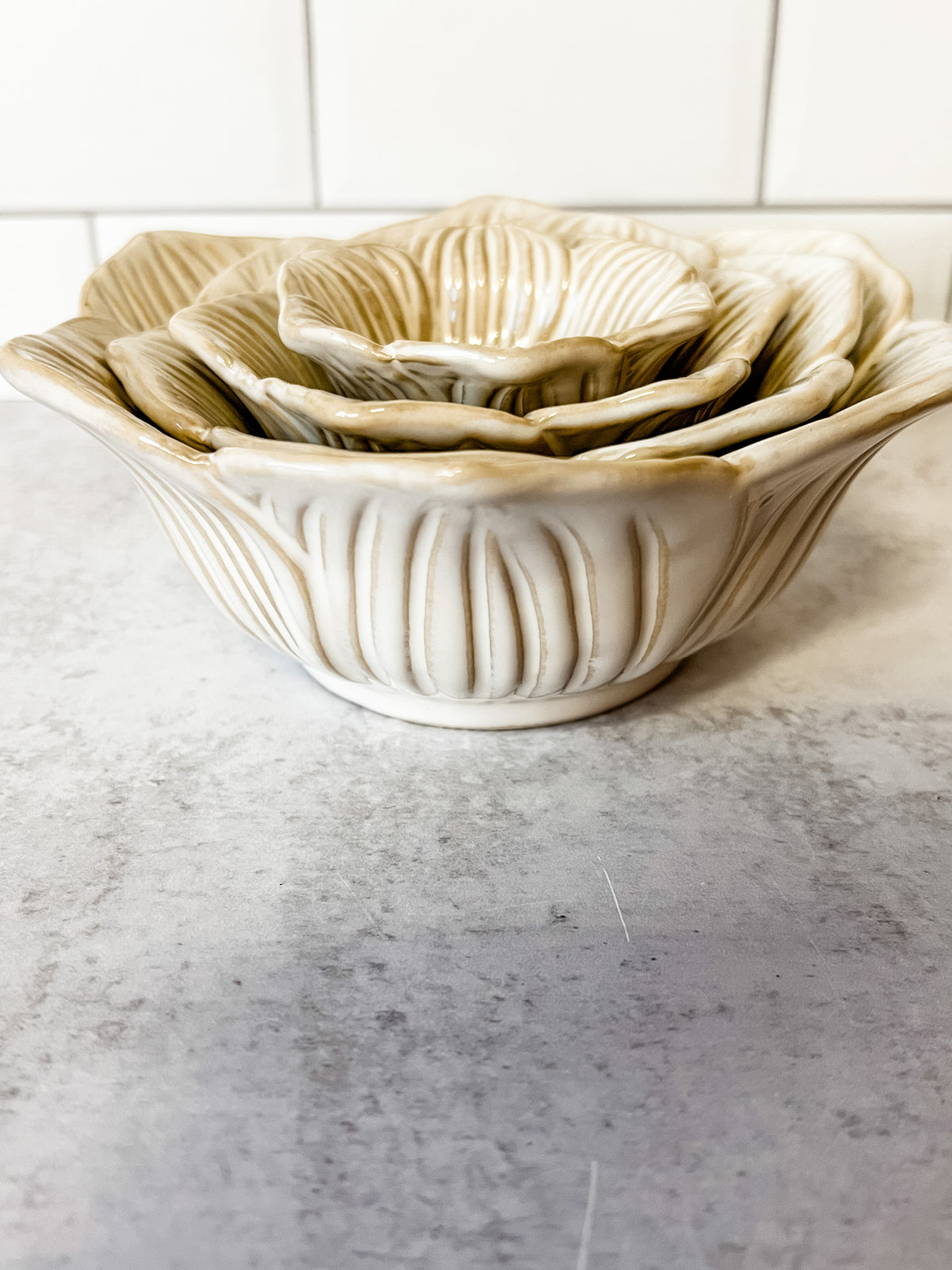 A set of nested ceramic bowls with a ribbed, lotus-petal design, shown on a gray stone surface with a white tiled background at the rustic barn in killingworth ct