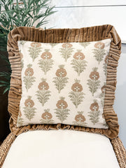 A square decorative throw pillow with a cream background and a brown botanical pattern, framed by a wide brown ruffled velvet border, displayed on a woven chair at the rustic barn in killingworth ct
