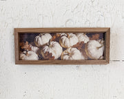 A rectangular wooden framed wall art piece featuring a printed still life of white pumpkins and brown leaves, mounted on a textured white wall.  At the rustic barn in Killingworth Ct